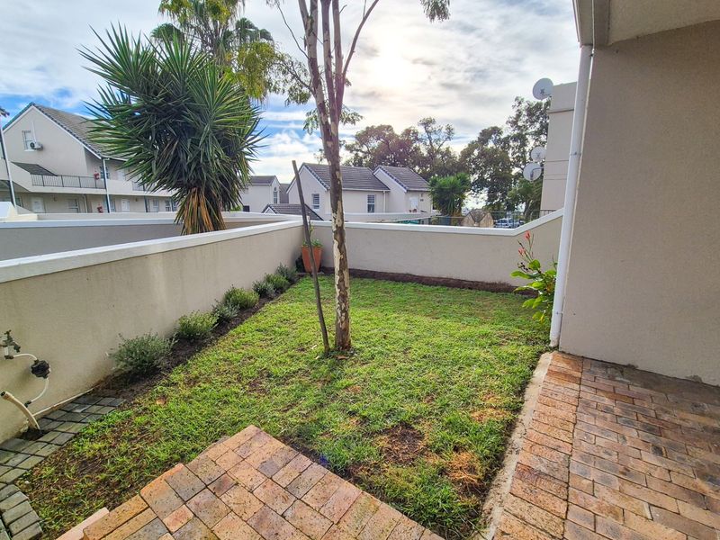A private rear garden area featuring a paved patio, boundary walls, and a small lawn space with an external water tap.