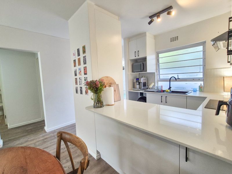 Modern kitchen featuring white cabinetry, quartz countertops, a black mixer tap, and integrated extractor fan, with an open-plan layout and track lighting.