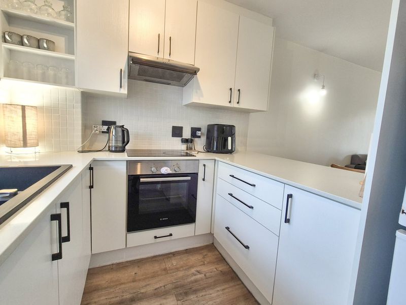 Modern kitchen featuring white cabinetry, integrated oven and hob, tiled backsplash, and durable laminate flooring in a clean, functional layout.