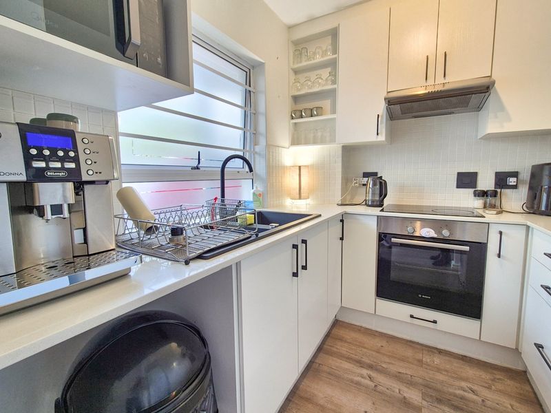 A modern, compact kitchen featuring white cabinetry, integrated appliances including an oven and hob, tiled backsplash, and durable laminate flooring.