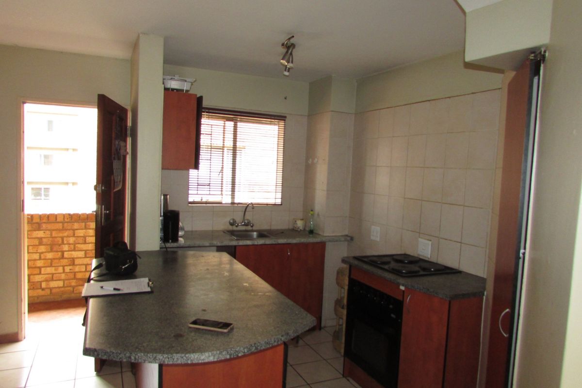 Functional kitchen featuring a breakfast bar, built-in oven and hob, tiled flooring, and direct access to an outdoor balcony area.