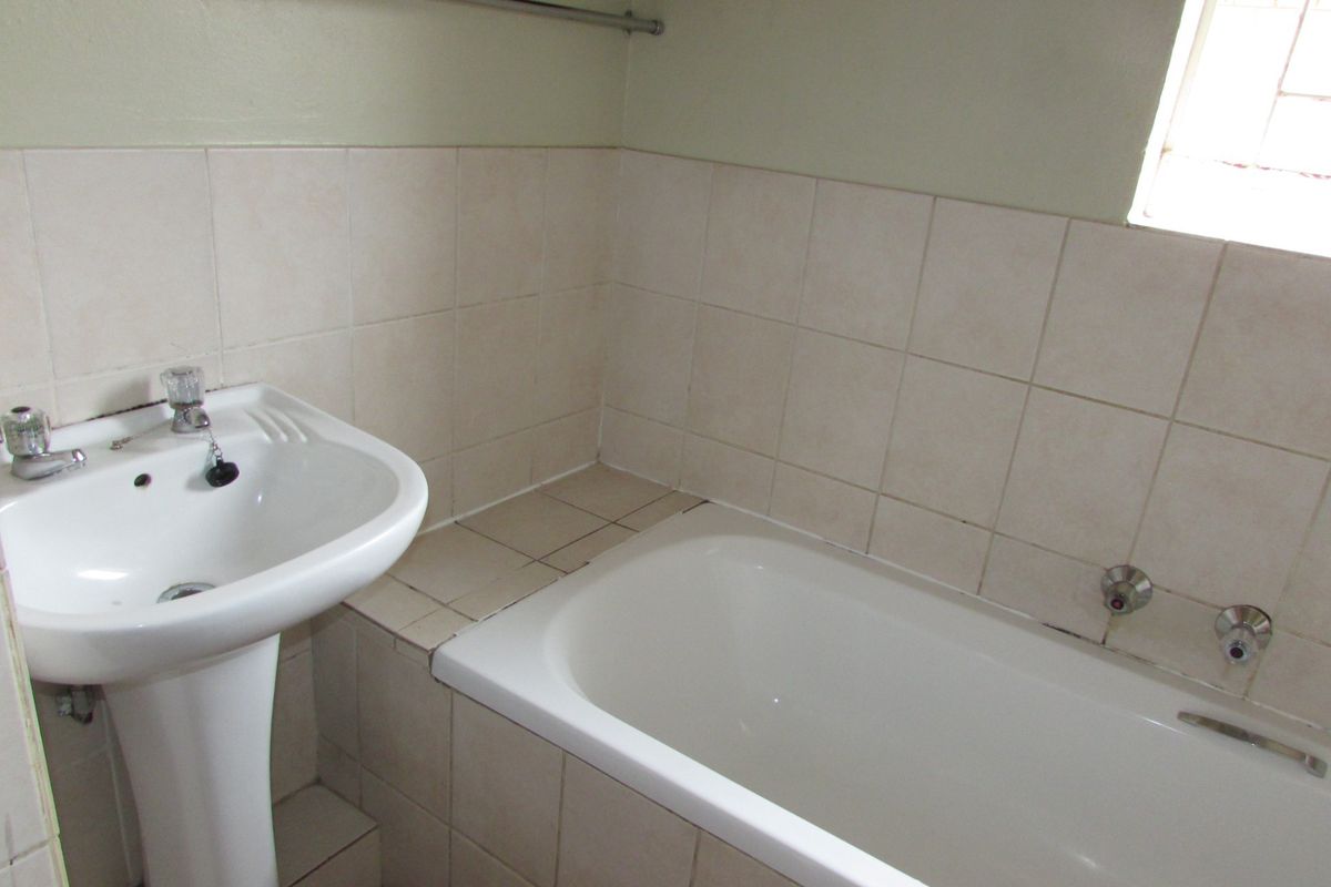 A functional bathroom featuring a white pedestal basin, a built-in bathtub with wall-mounted taps, and neutral wall tiling.