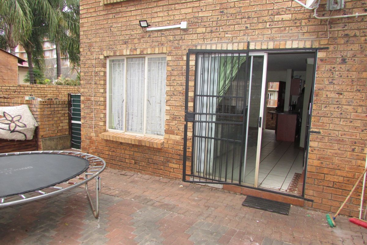 Rear view of the apartment featuring a brick facade, paved patio area, and a sliding glass door with security gate access.
