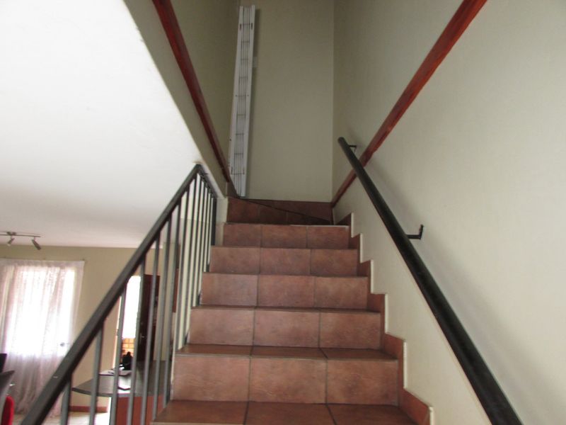 A staircase featuring tiled steps, a metal balustrade, and a wall-mounted handrail, providing access between levels in the apartment.