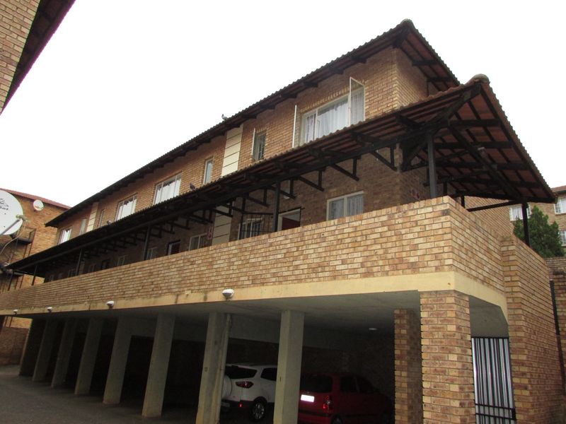 Exterior view of a multi-story apartment building featuring face-brick facade, covered balcony, and ground-level parking area.