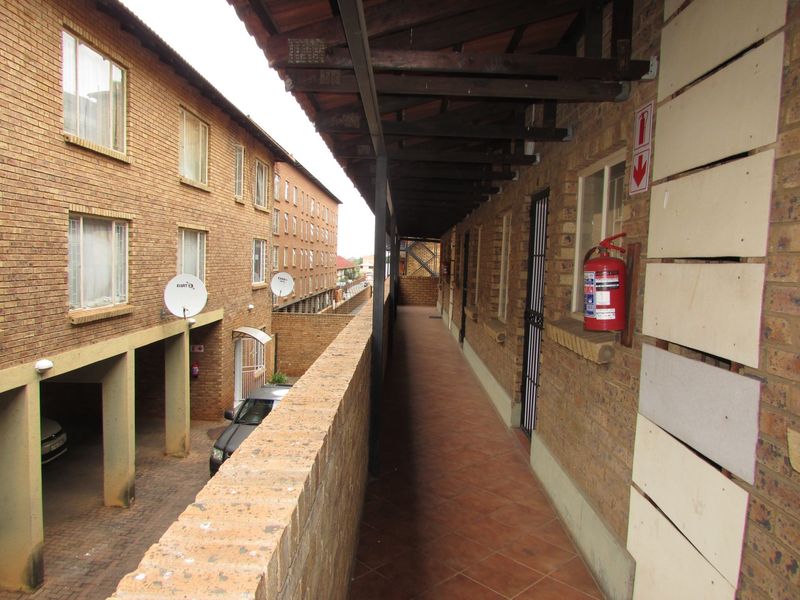 An exterior walkway corridor featuring tiled flooring, a timber-framed roof structure, and brick wall finishes, providing access to apartment units.