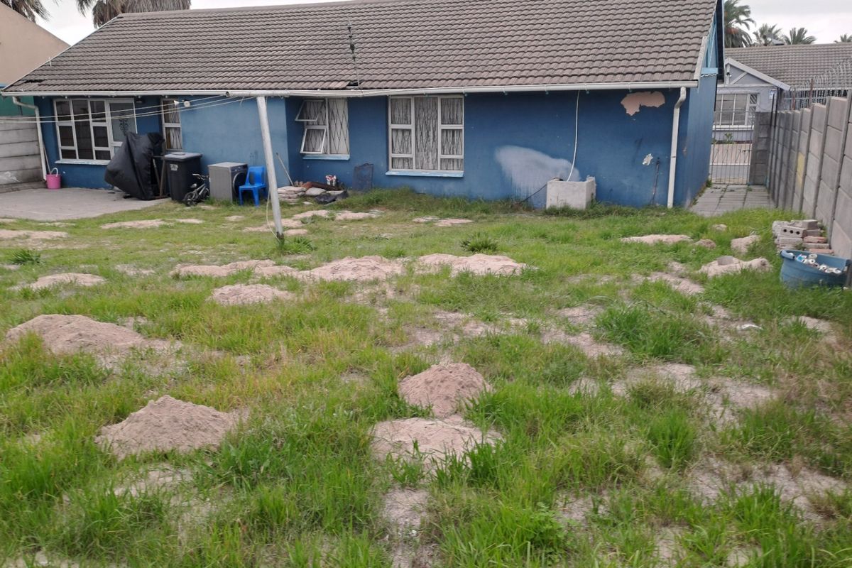 Rear view of a detached house featuring a large, unmaintained garden area with significant landscaping required and visible exterior wall damage.