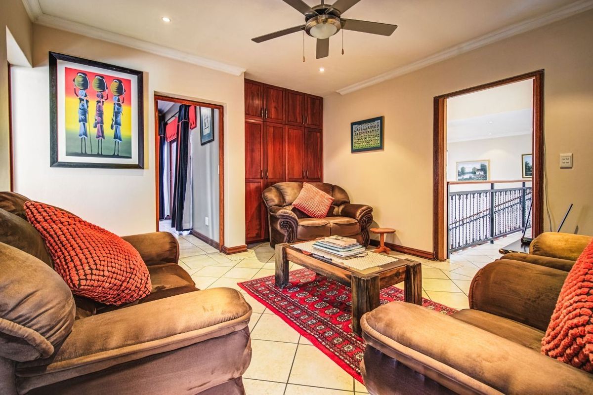 A cozy living room featuring tiled flooring, built-in wooden cabinetry, and a ceiling fan, providing access to adjacent rooms and a hallway.