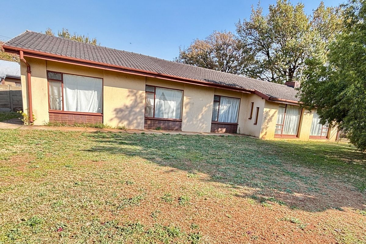Rear view of a single-story residential house featuring a tiled roof, large windows, and a spacious backyard area.
