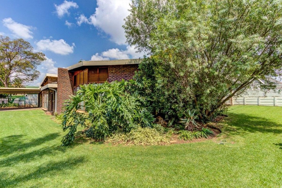 A view of the rear exterior of the house, featuring brick facade, established garden landscaping, and a lawn area.
