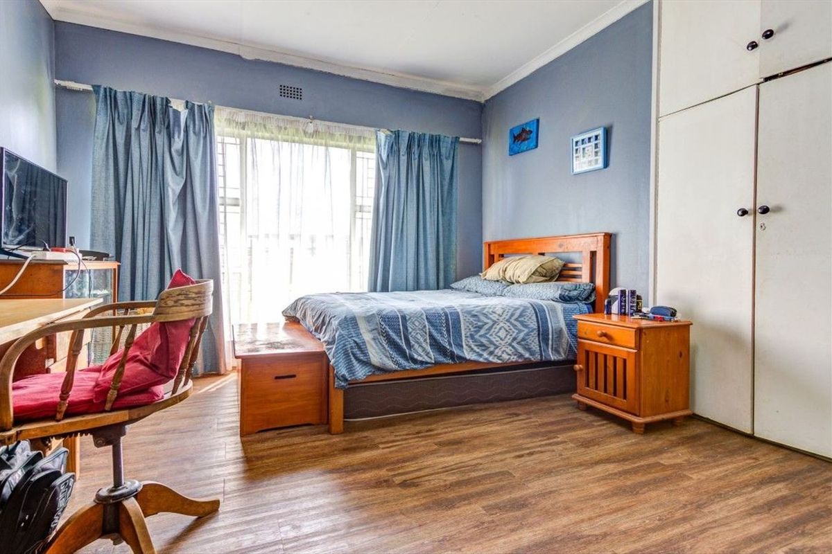 A bedroom featuring built-in cupboards, wood-look flooring, and large windows with curtains, providing natural light and functional storage space.