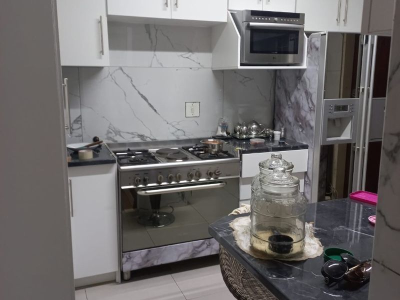 Modern kitchen featuring white cabinetry, marble-look splashback, stone countertops, and a stainless steel gas stove with integrated extractor fan.
