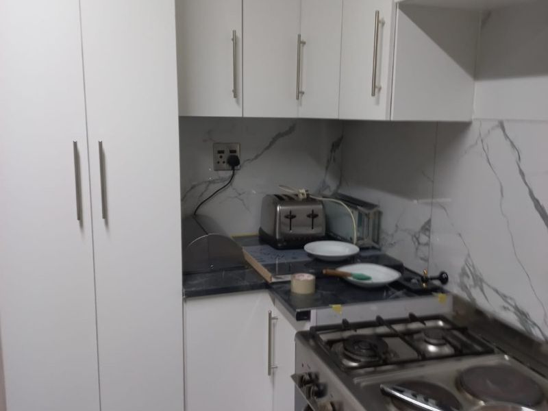Modern kitchen featuring white cabinetry, marble-look splashback, and a stainless steel gas stove with integrated extractor.