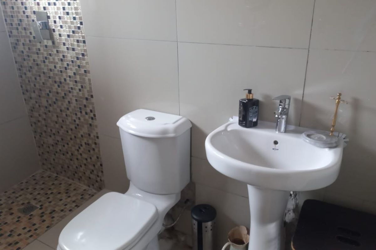 A functional bathroom featuring a pedestal basin, toilet, and a shower area with decorative mosaic tile accents.