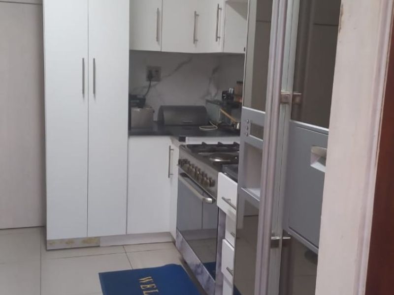 A compact, modern kitchen featuring white cabinetry, stone countertops, and a built-in gas stove with oven, finished with neutral floor tiles.
