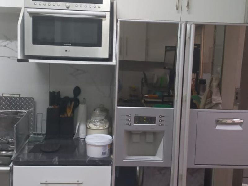 A compact kitchen area featuring white cabinetry, a built-in microwave, and a modern integrated refrigerator with a mirrored finish.