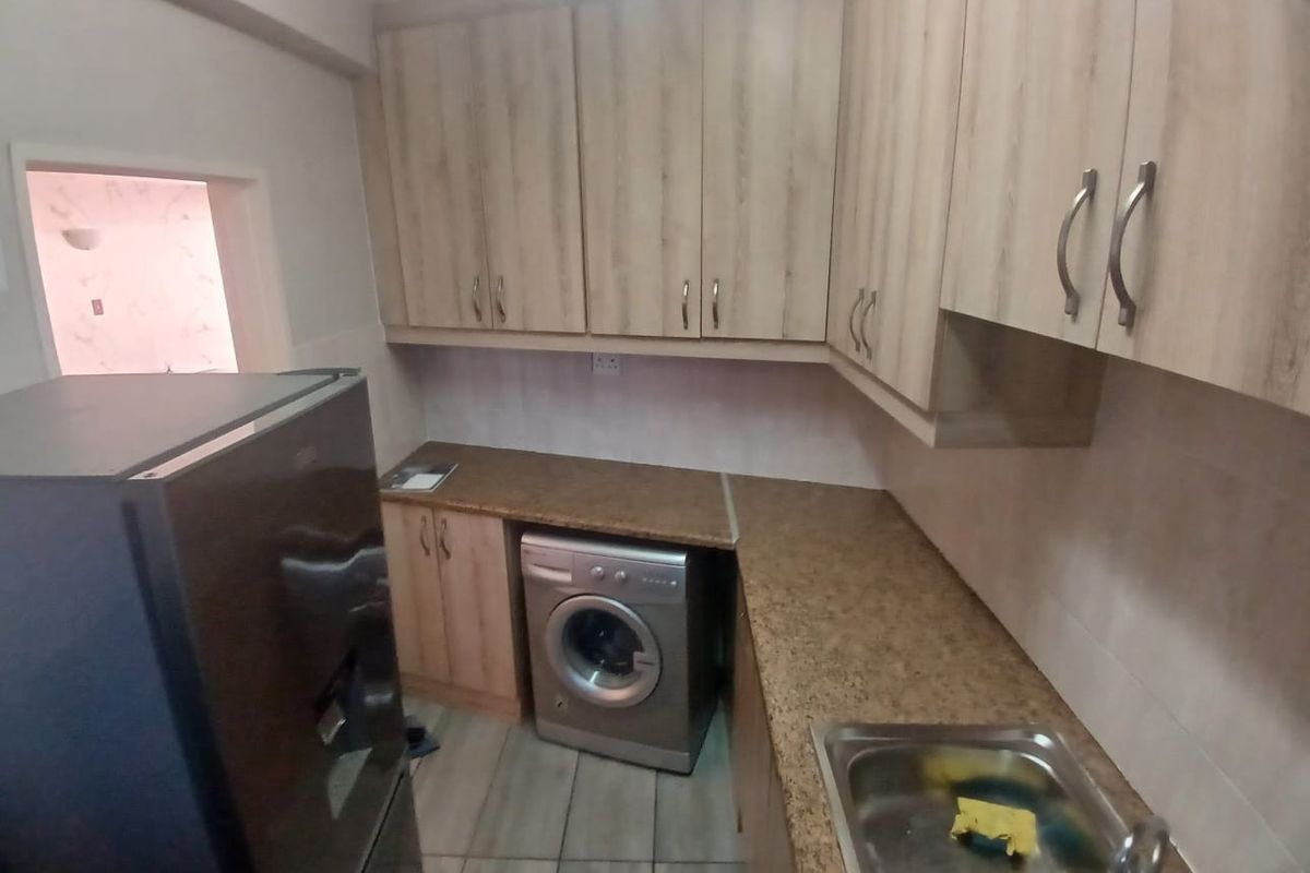 A functional kitchen featuring light wood-look cabinetry, granite-style countertops, a stainless steel sink, and space for a washing machine.