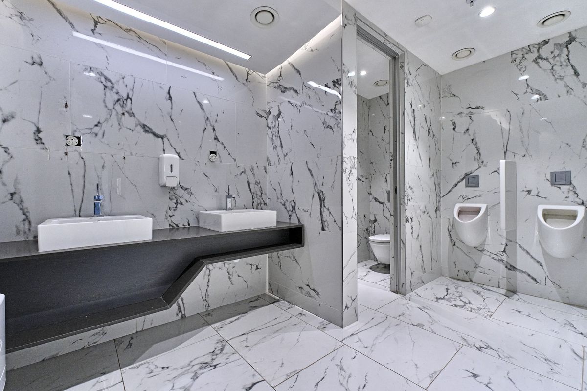 Modern commercial restroom featuring high-end marble wall and floor tiling, dual vessel sinks, and wall-mounted urinals with integrated lighting.