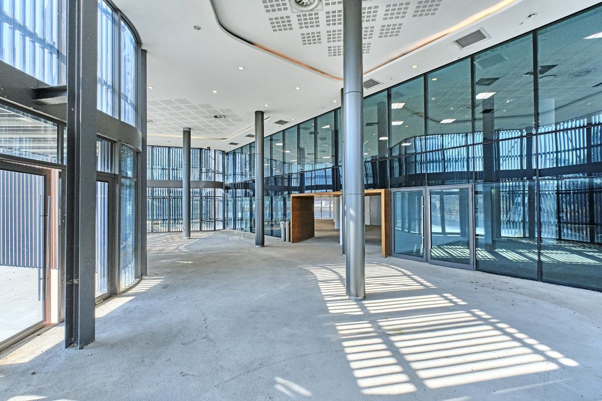Spacious modern commercial entrance lobby featuring extensive floor-to-ceiling glass curtain walls, structural steel columns, and a contemporary suspended ceiling design.