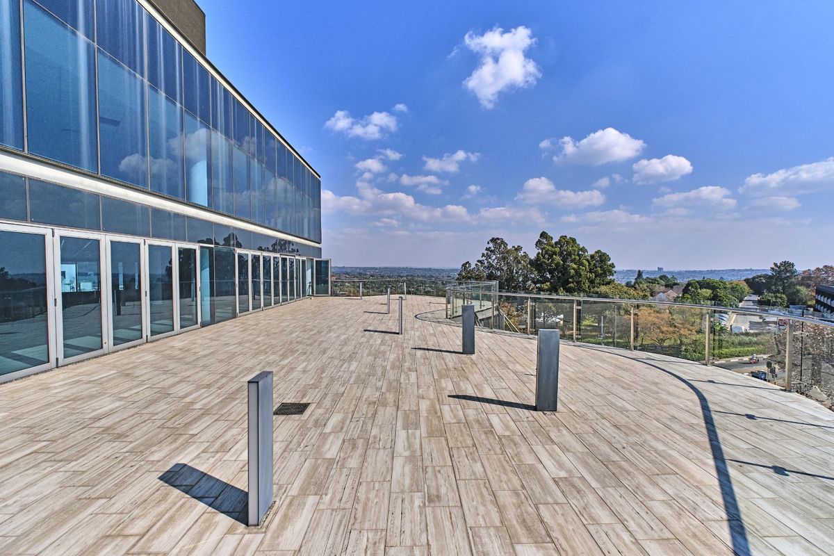 Expansive outdoor balcony featuring modern glass balustrades, tiled flooring, and integrated bollard lighting, offering panoramic views from the commercial building.