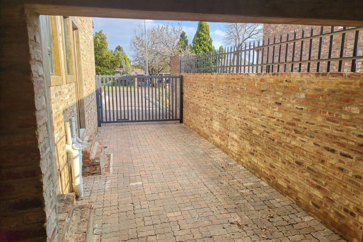 A secure side access area featuring brick paving, a high perimeter brick wall with metal security fencing, and a gated entrance.