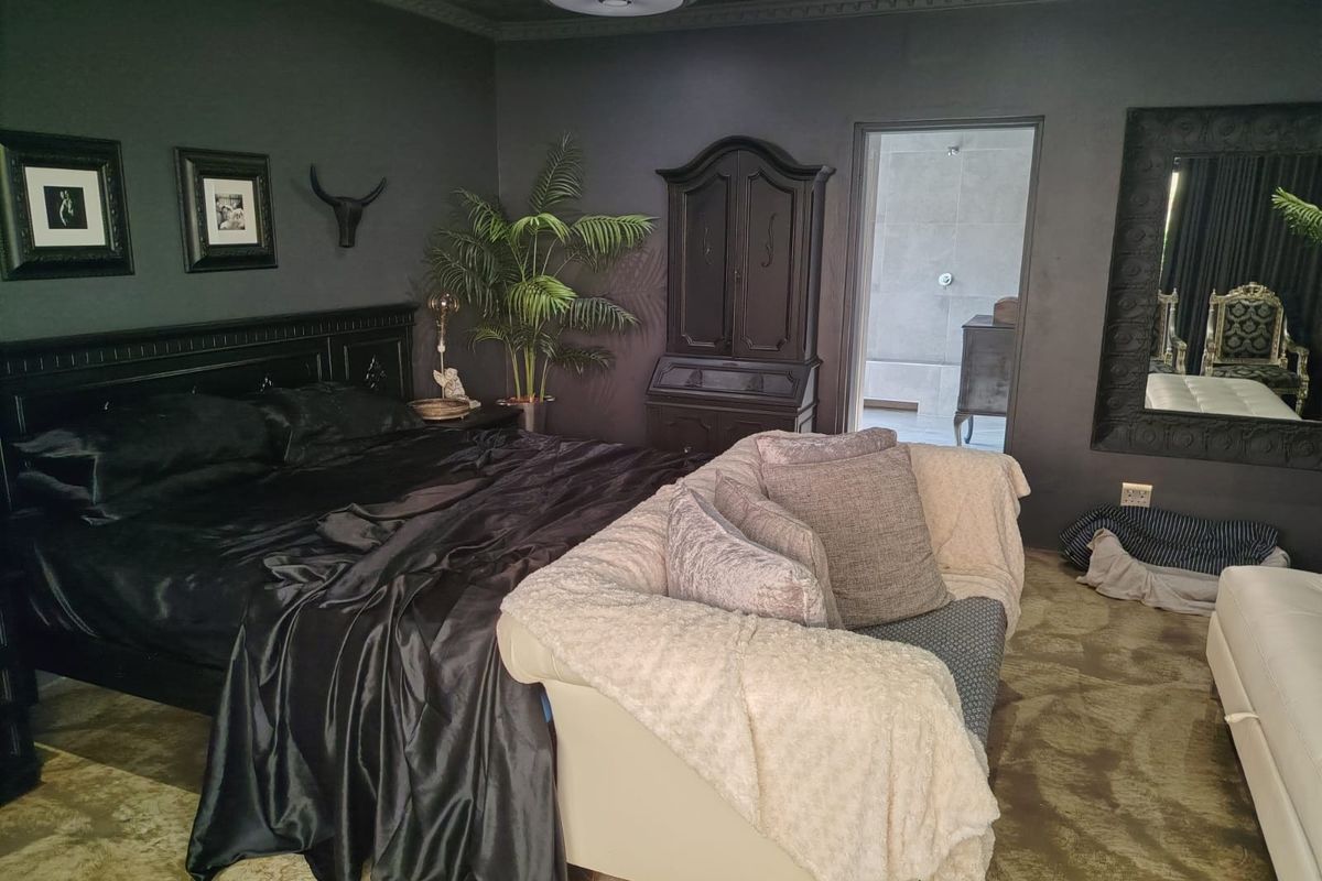 A bedroom featuring dark-toned walls, decorative ceiling molding, and an adjoining bathroom, creating a moody and intimate atmosphere.