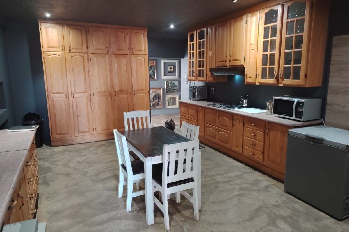 Spacious kitchen featuring extensive wooden cabinetry, built-in stove with extractor fan, and ample storage space, finished with a dark ceiling and concrete flooring.