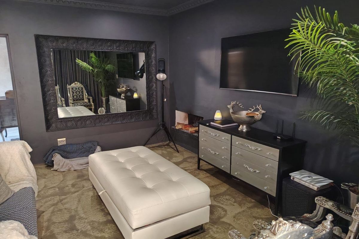A dark-themed living room featuring a built-in fireplace, decorative crown molding, and a large wall-mounted mirror.