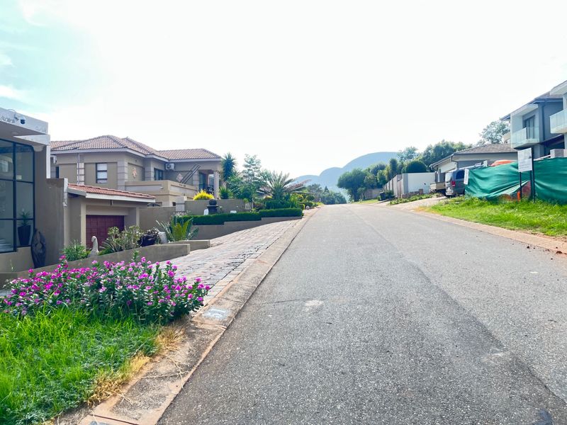 A view looking down a paved residential street in a well-maintained estate, featuring surrounding homes and distant mountain views.
