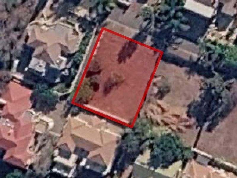 An aerial view of a vacant residential plot highlighted in red, situated within an established suburban neighborhood.