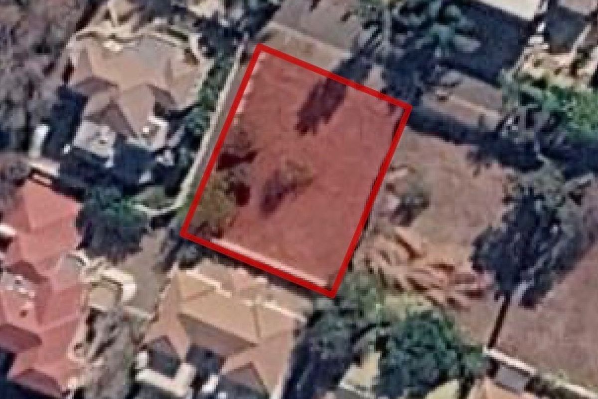 An aerial view of a vacant residential plot highlighted in red, situated within an established suburban neighborhood.