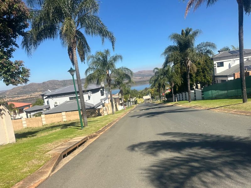 A view looking down a paved residential street in a well-maintained estate, featuring mature palm trees and surrounding residential properties.