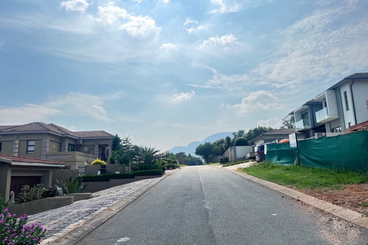 A view looking down a paved residential street in a developed neighborhood, featuring surrounding modern homes and distant mountain views.