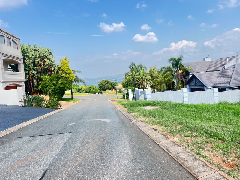 A view looking down a paved residential street in a well-maintained estate, featuring surrounding homes and distant landscape views.