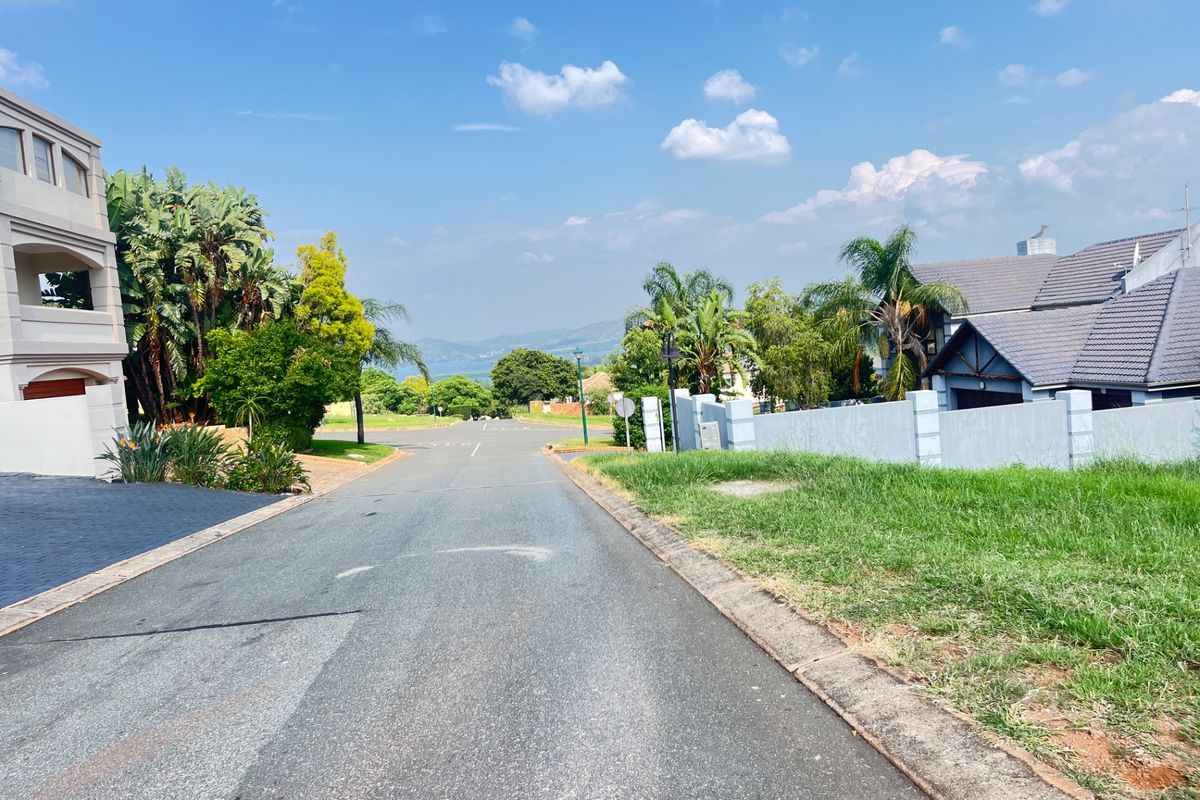 A view looking down a paved residential street in a well-maintained estate, featuring surrounding homes and distant landscape views.