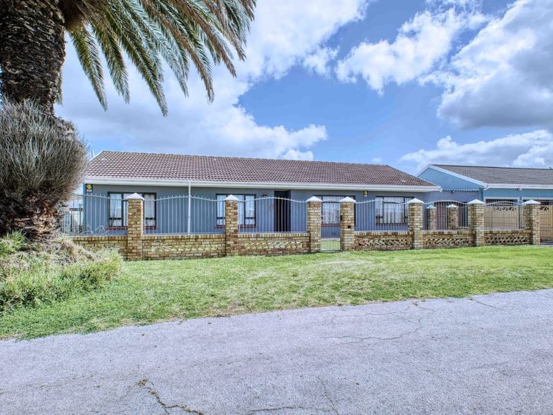 Front elevation of a single-story house featuring a tiled roof, grey exterior walls, and a secure brick and metal perimeter fence.