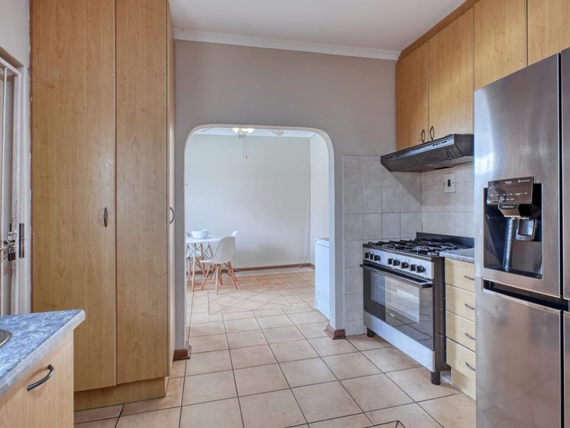 A functional kitchen featuring wooden cabinetry, a gas stove with extractor fan, and tiled flooring, leading through an archway to an adjacent living area.