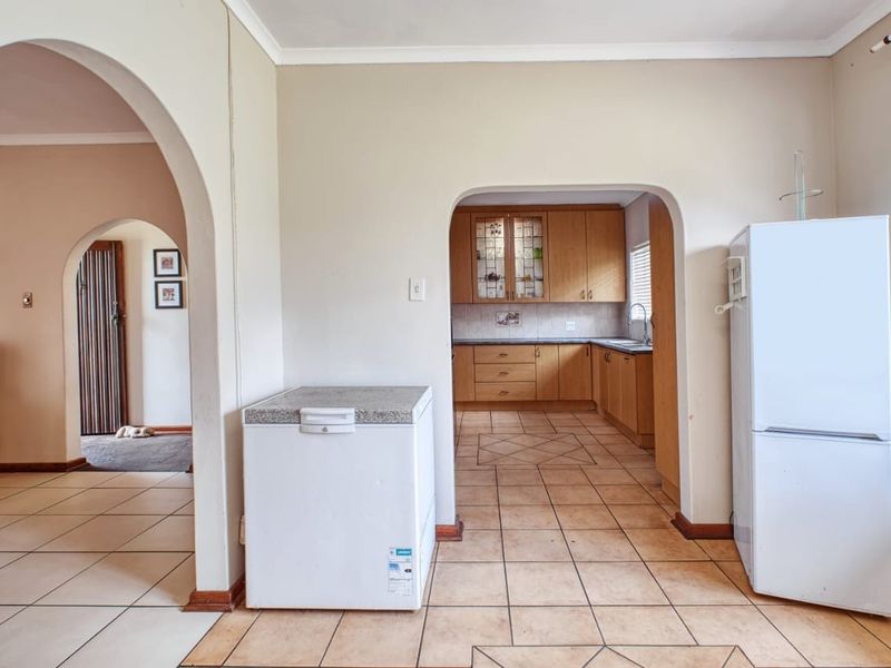Open plan living area featuring arched doorways and a view into a functional kitchen with wooden cabinetry and tiled flooring.