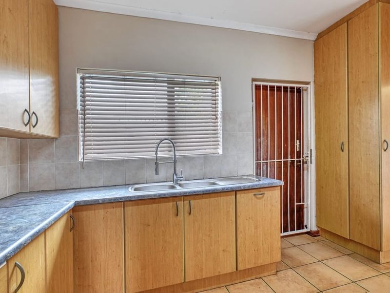 A functional kitchen featuring light wood-look cabinetry, laminate countertops, a double sink, and tiled flooring with direct access to an exterior security door.