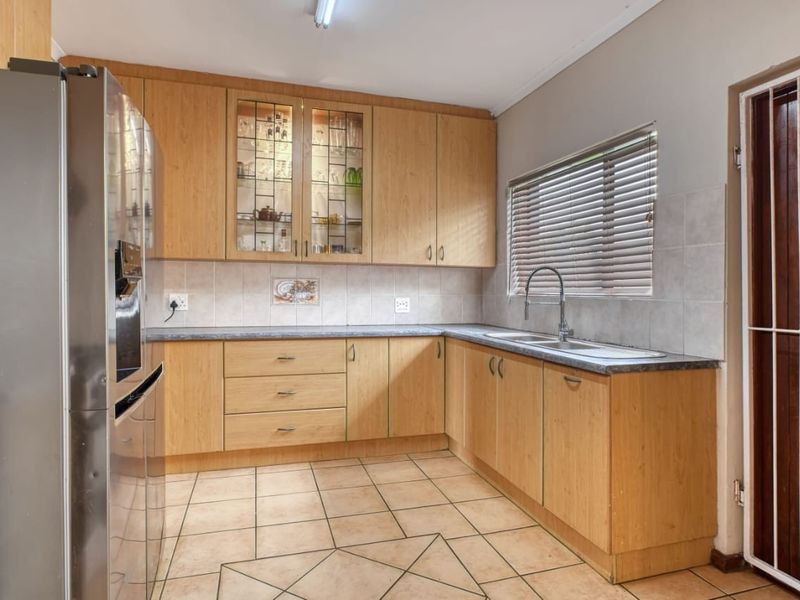 A functional kitchen featuring light wood-finish cabinetry, laminate countertops, a double sink, and tiled flooring with a neutral splashback.