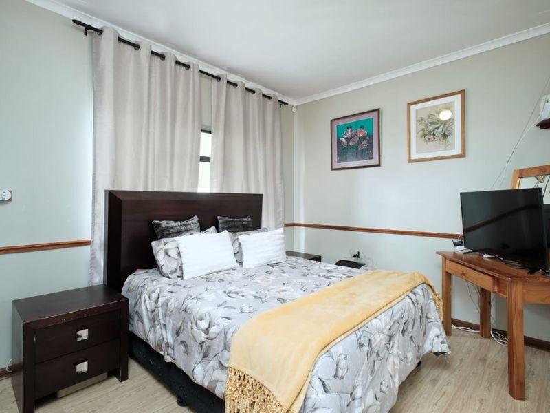 A well-maintained bedroom featuring light-toned laminate flooring, neutral wall paint, and classic chair rail detailing.
