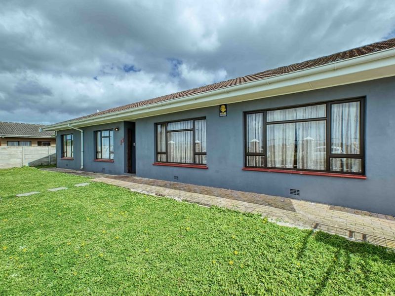 Rear exterior view of the house featuring a paved walkway, well-maintained lawn, and dark aluminium window frames under a tiled roof.