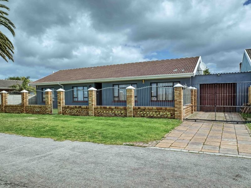 Front view of a single-story house featuring a paved driveway, secure metal fencing, brick boundary wall, and a tiled roof.