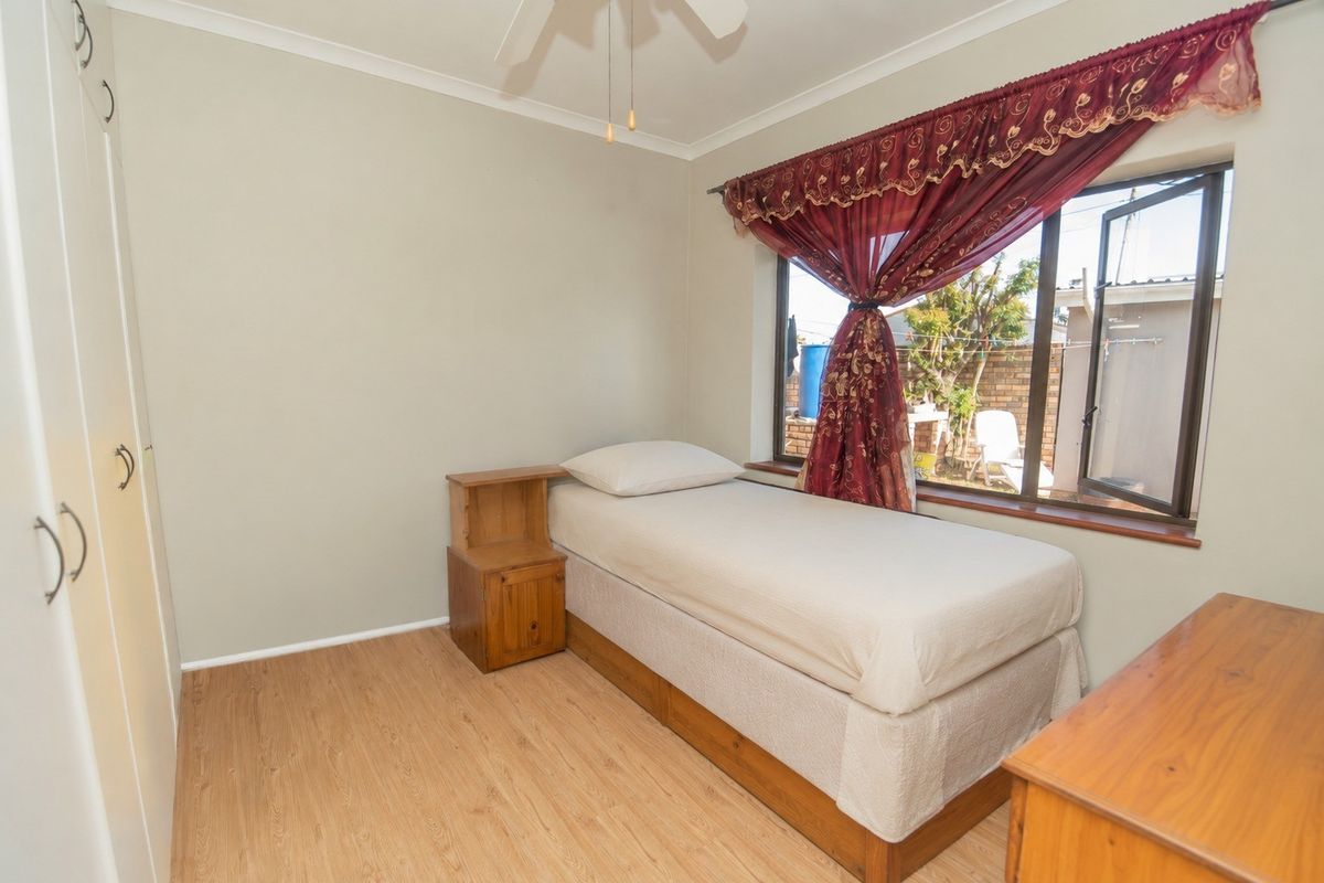 A bedroom featuring light wood-look flooring, built-in cupboards, and a window with views of the rear exterior area.