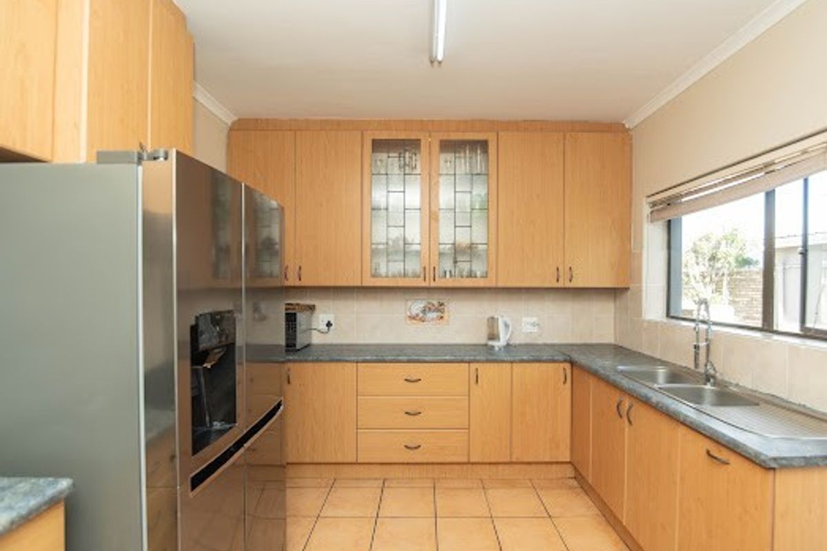 A functional kitchen featuring light wood cabinetry, laminate countertops, a double stainless steel sink, and tiled flooring with ample storage space.