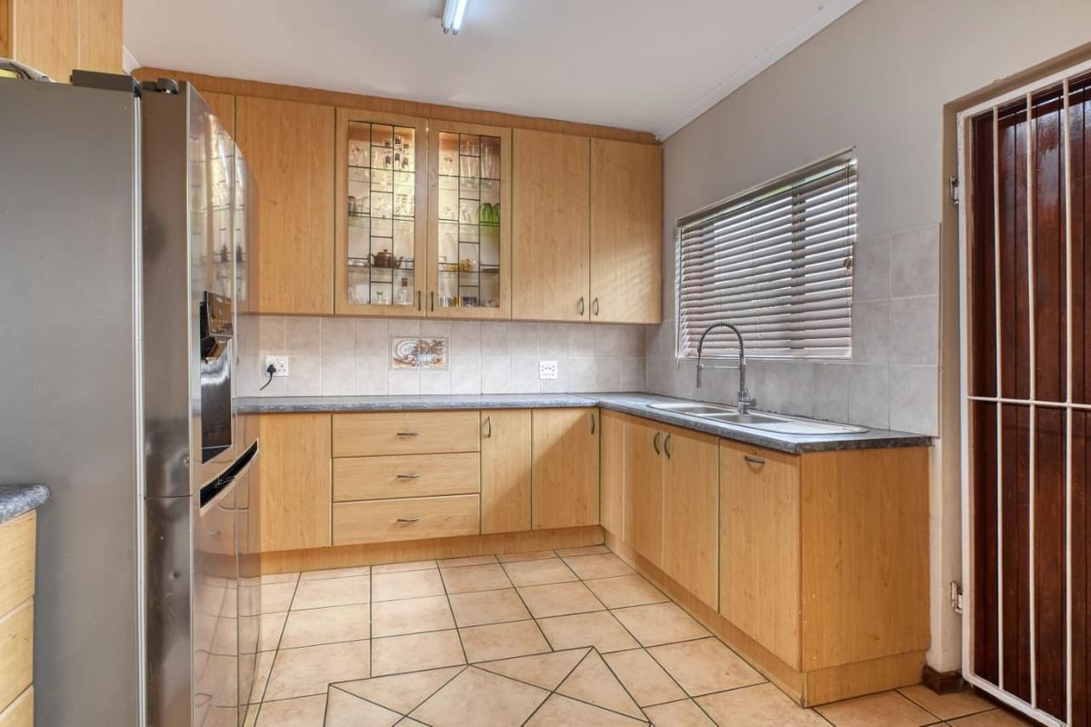 A functional kitchen featuring light wood-finish cabinetry, laminate countertops, a double sink, and tiled flooring with a neutral splashback.