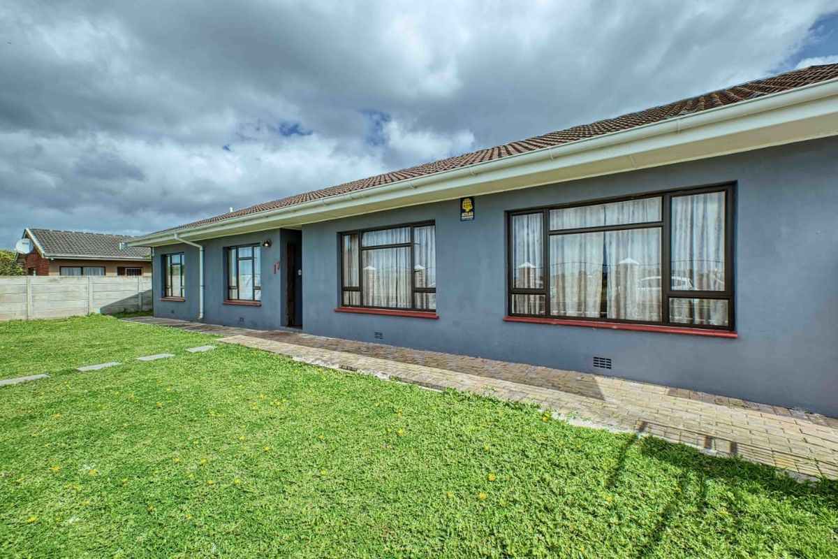 Rear exterior view of the house featuring a paved walkway, well-maintained lawn, and dark aluminium window frames under a tiled roof.