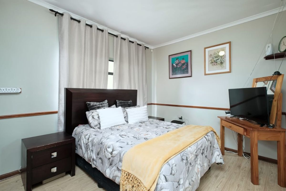 A well-maintained bedroom featuring light-toned laminate flooring, neutral wall paint, and classic chair rail detailing.