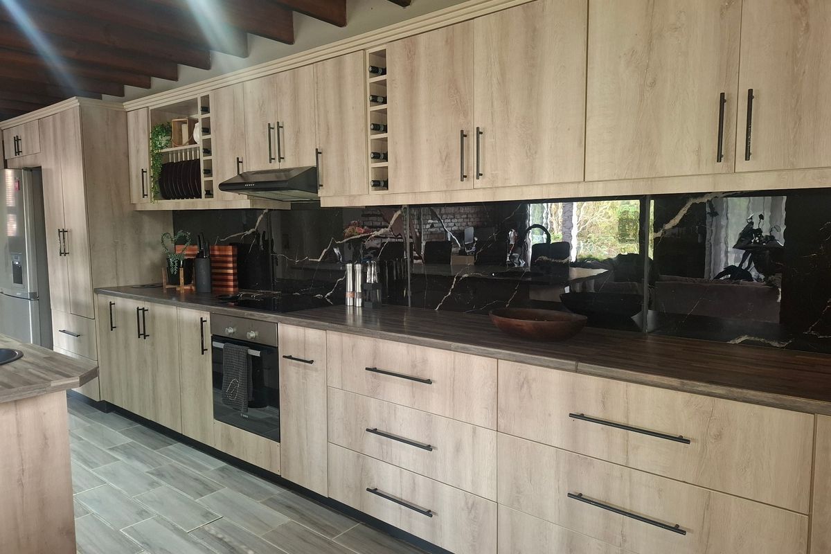 Modern kitchen featuring light wood-grain cabinetry, dark marble-effect splashback, integrated oven, hob, and extractor fan, complemented by tiled flooring and exposed timber ceiling beams.