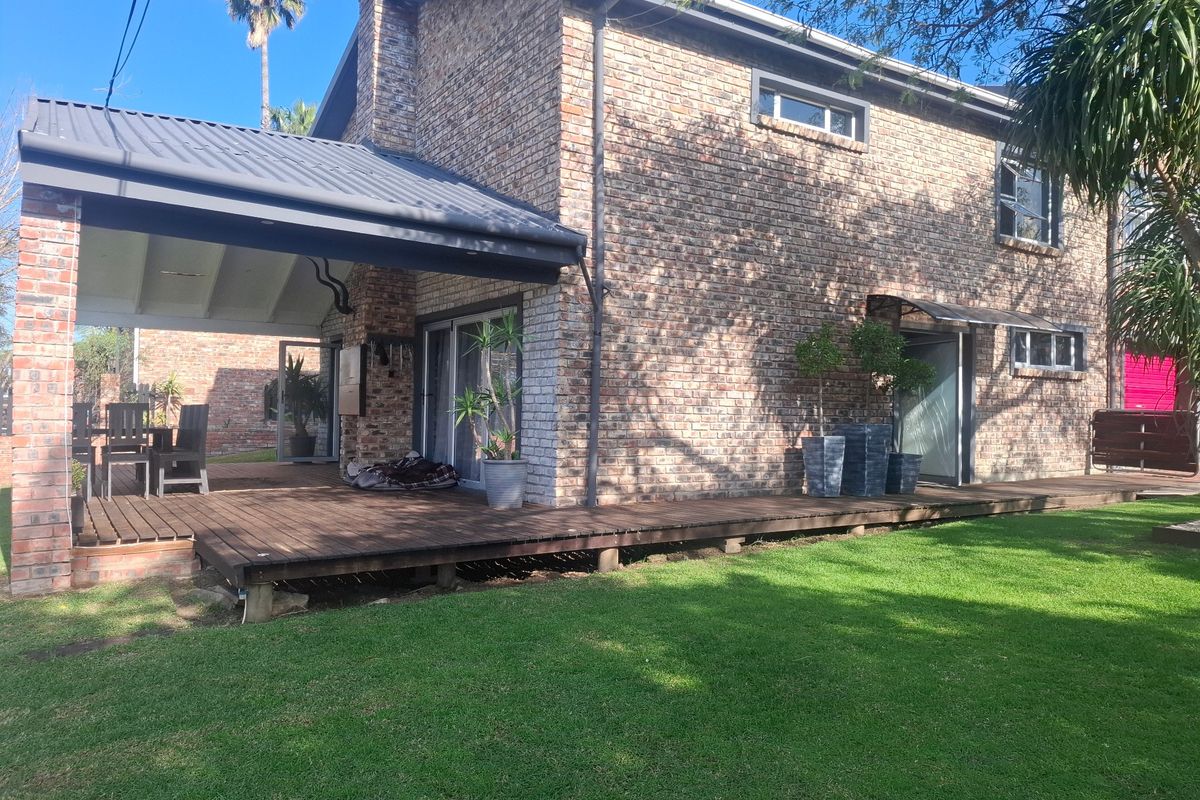 Rear view of a double-story brick house featuring a covered wooden deck patio, large lawn area, and sliding glass door access.